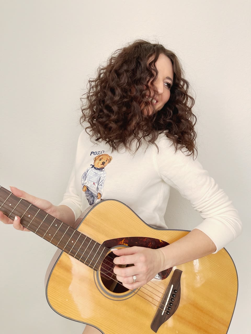 Shoulder-length, defined dark-brown curls on a woman holding an acoustic guitar