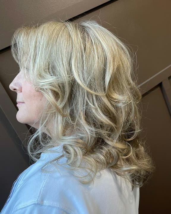 Shoulder-length blonde hair with lighter and darker strands, styled in loose curls, seen in profile
