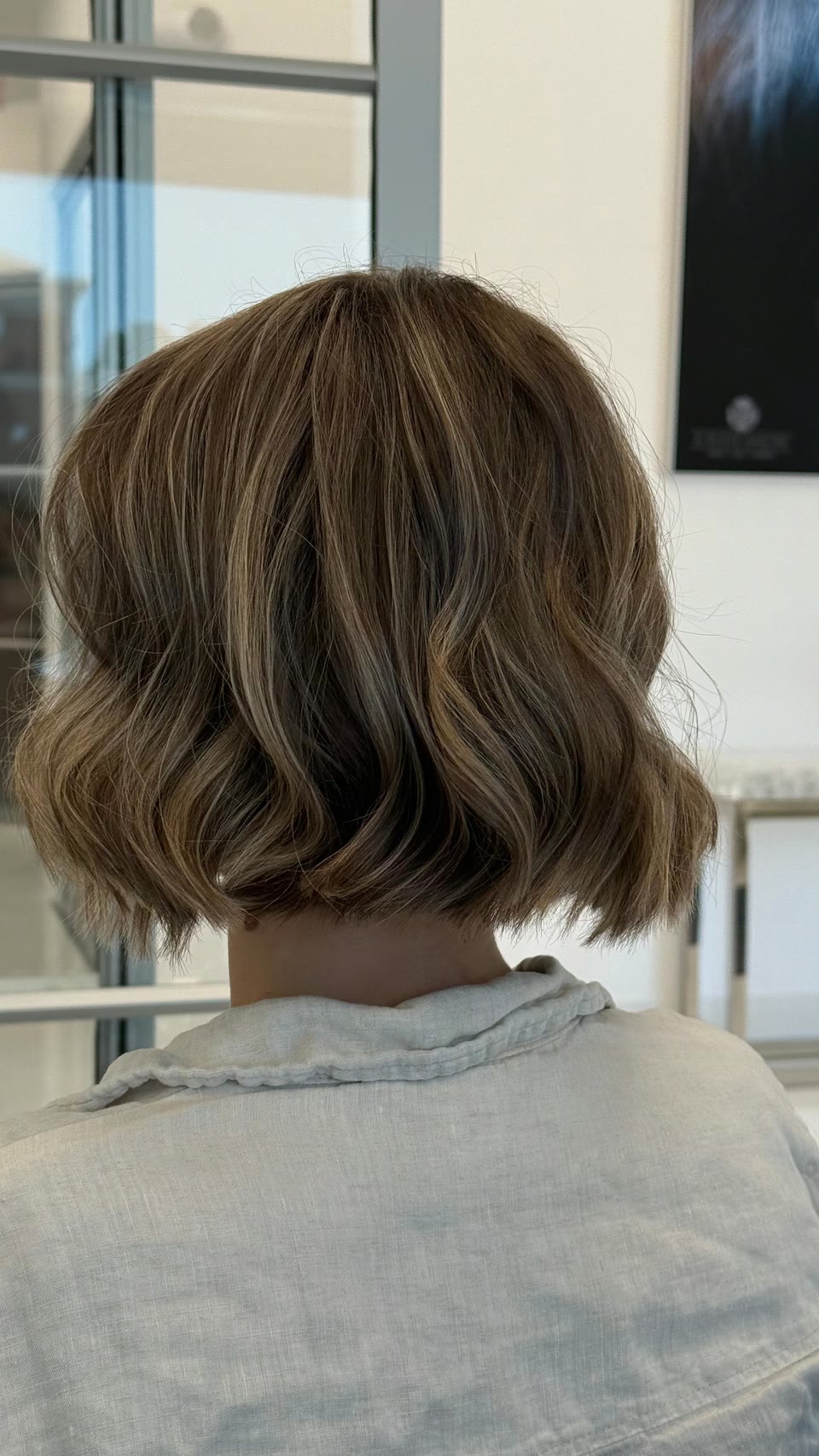 Short, wavy bob with caramel highlights on brown hair, seen from behind