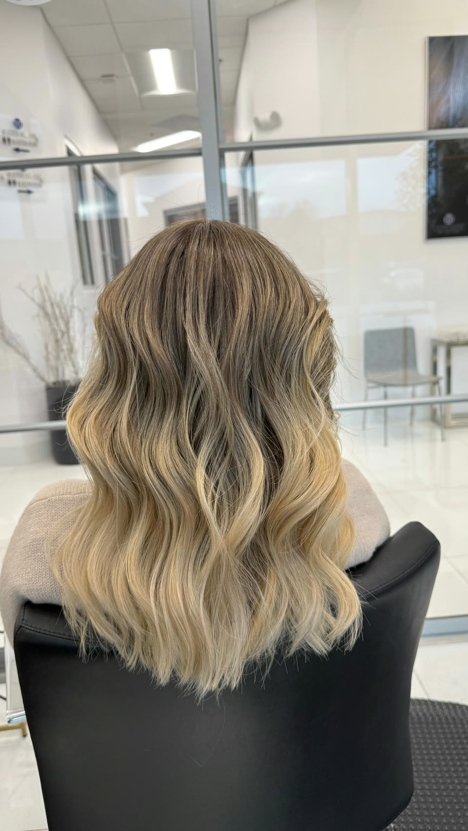 Medium-length wavy hair shading from an ash-brown root to light blonde ends, seen from behind