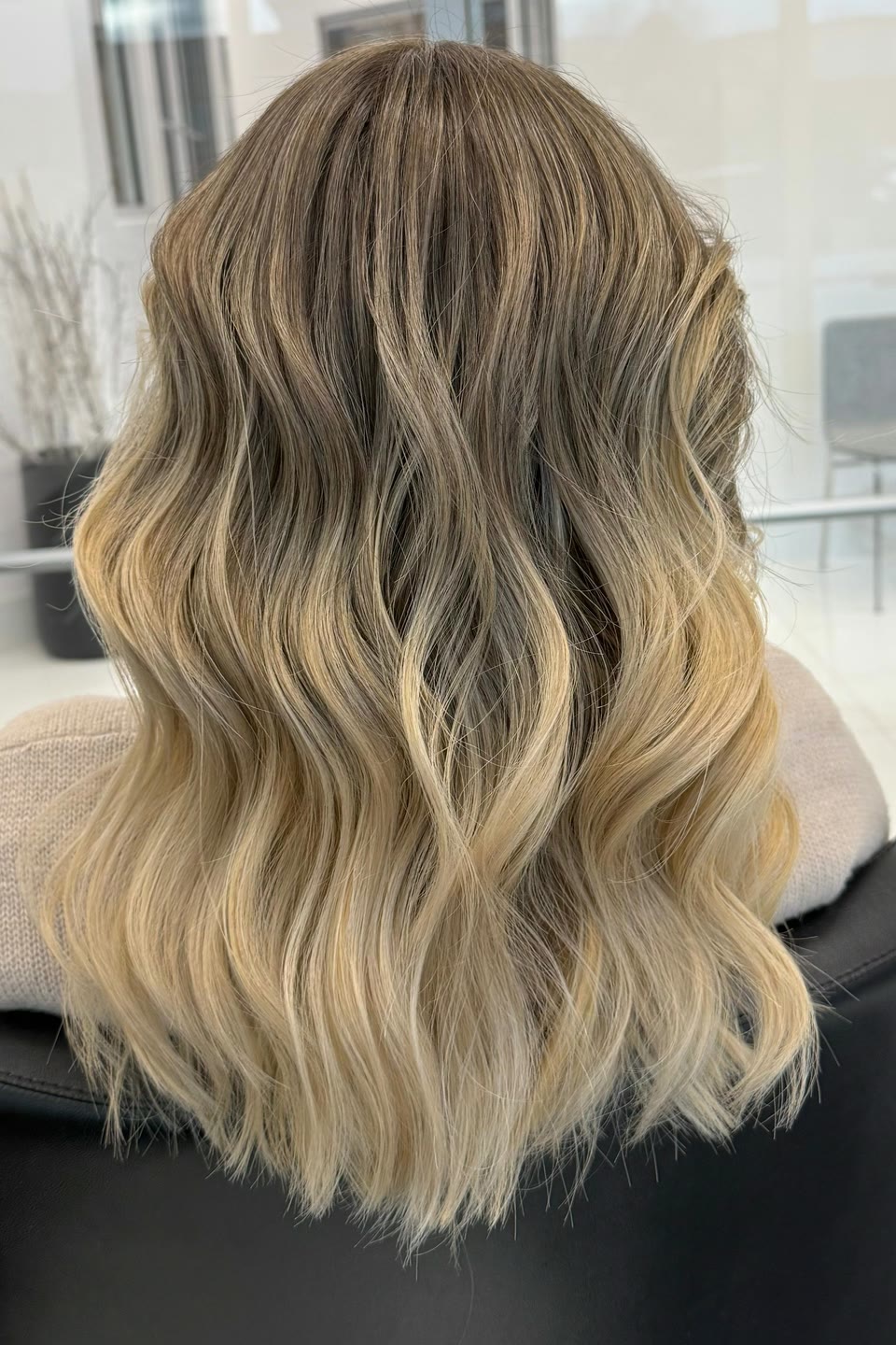 Medium-length wavy hair shading from an ash-brown root to light blonde ends, seen from behind