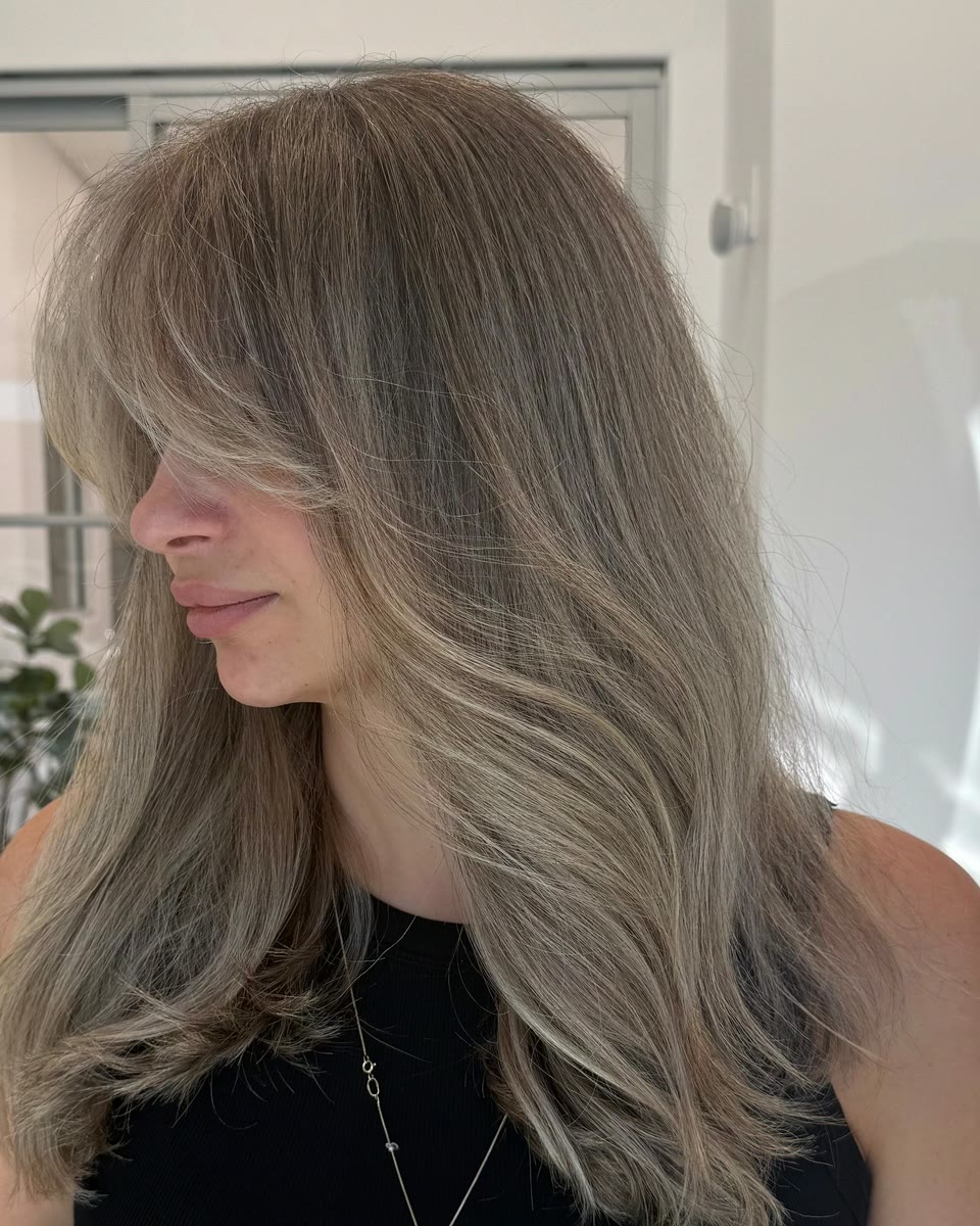 Long, ash-toned light-brown hair with lighter pieces and face-framing layers, seen from the side