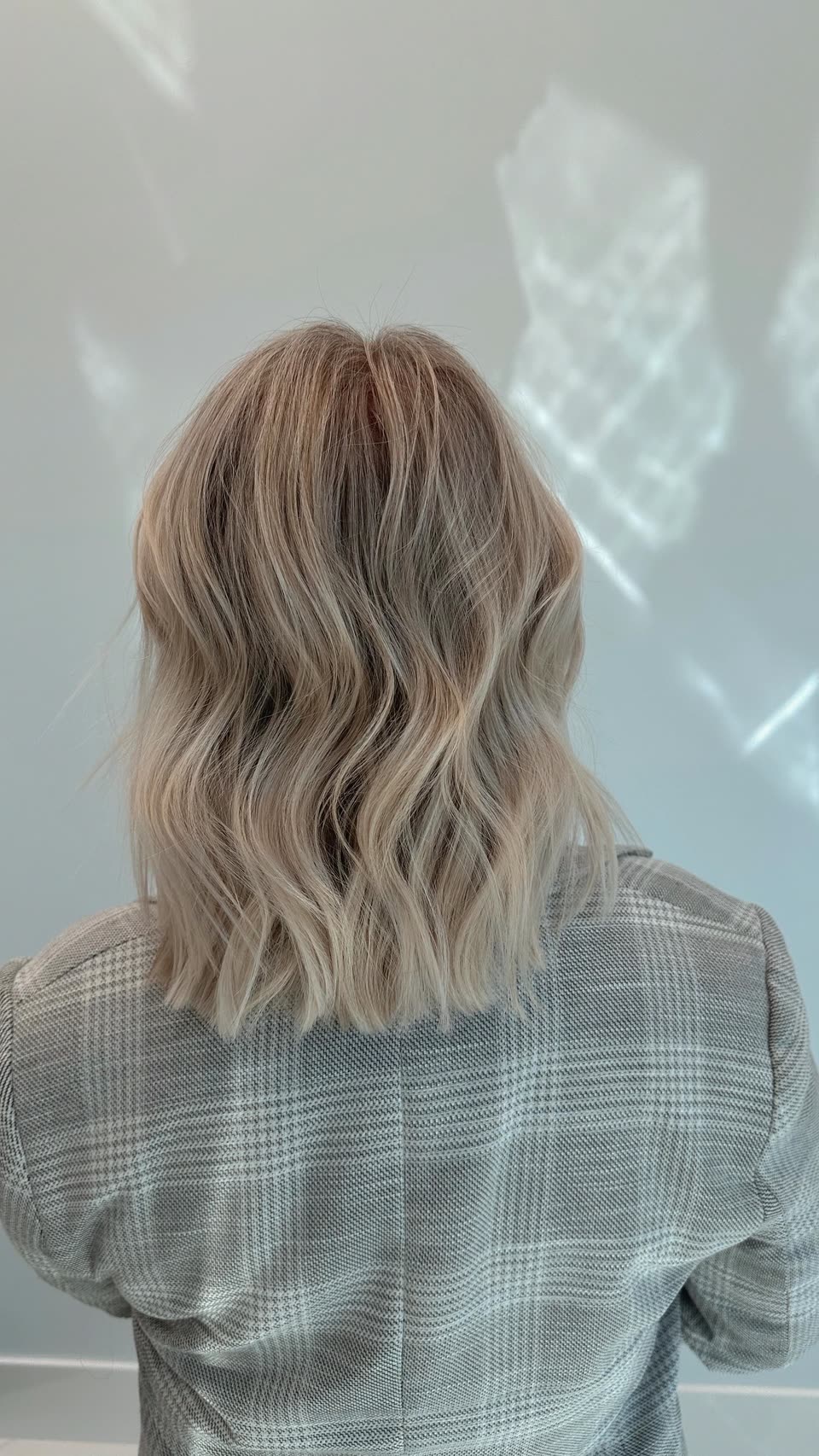 Shoulder-length beige-blonde hair with a slightly darker root, in soft waves, seen from behind