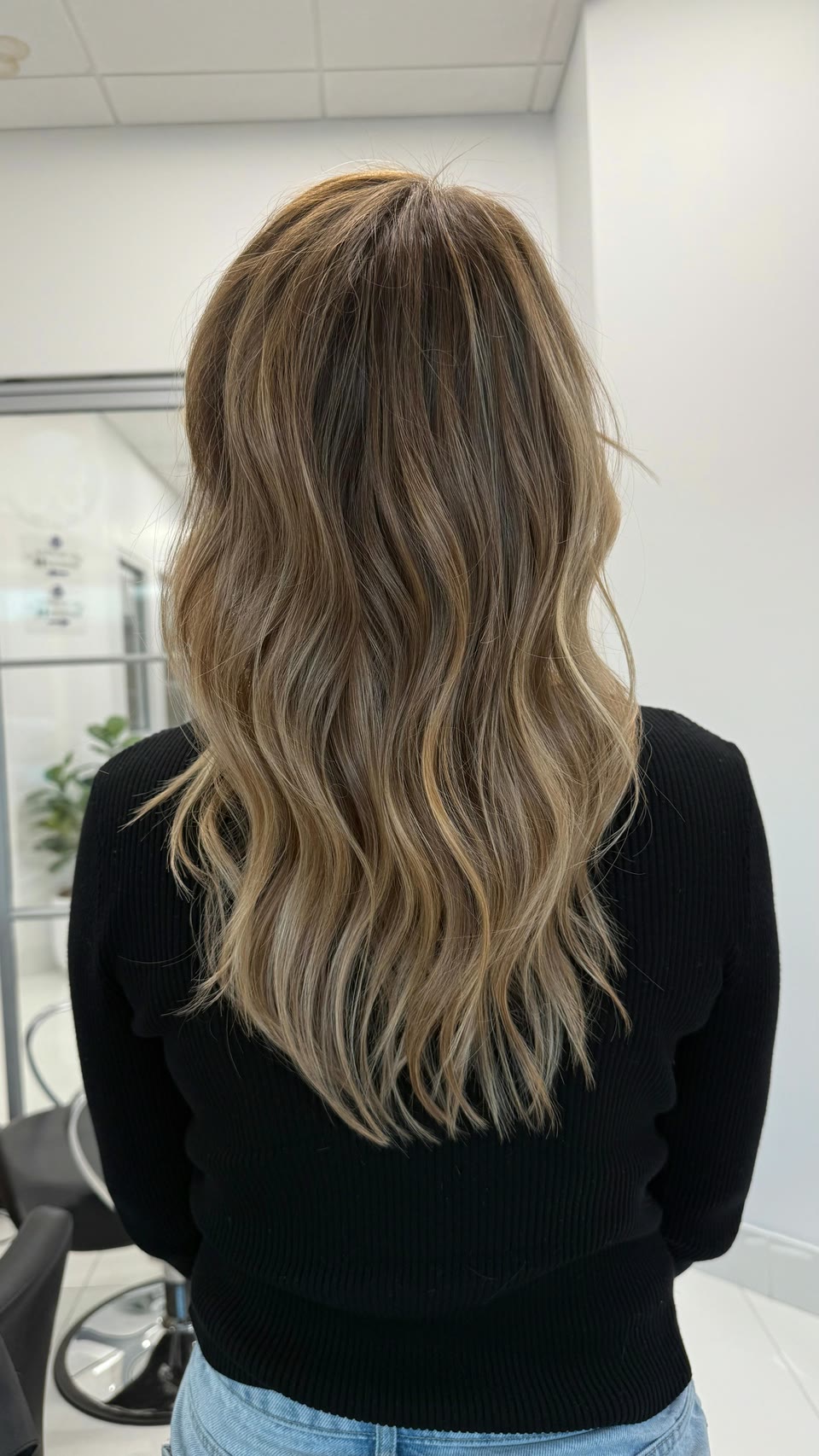 Long, wavy hair with a brown root blending into lighter golden-blonde lengths, seen from behind