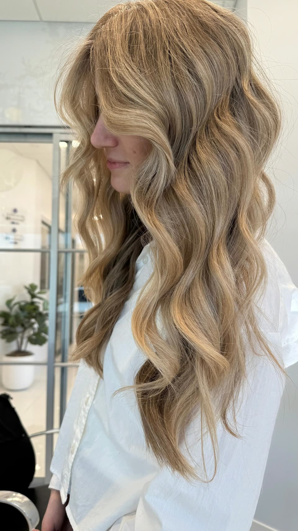 Long, voluminous honey-blonde waves with darker strands underneath, seen in profile