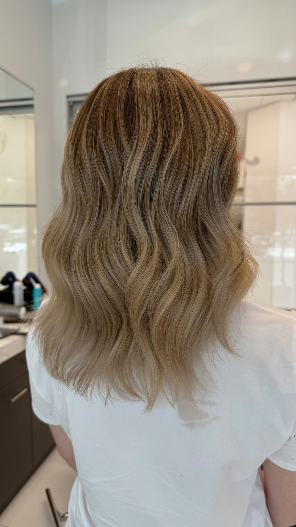 Medium-length golden-beige waves with a deeper root, seen from behind