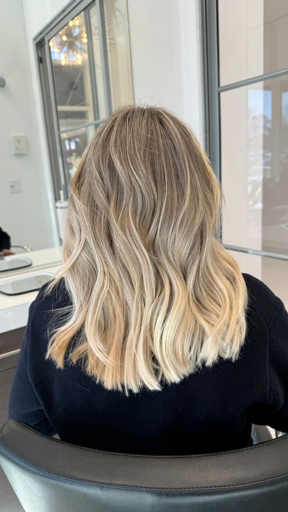Medium-length bronde hair blending into bright blonde ends, in loose waves, seen from behind