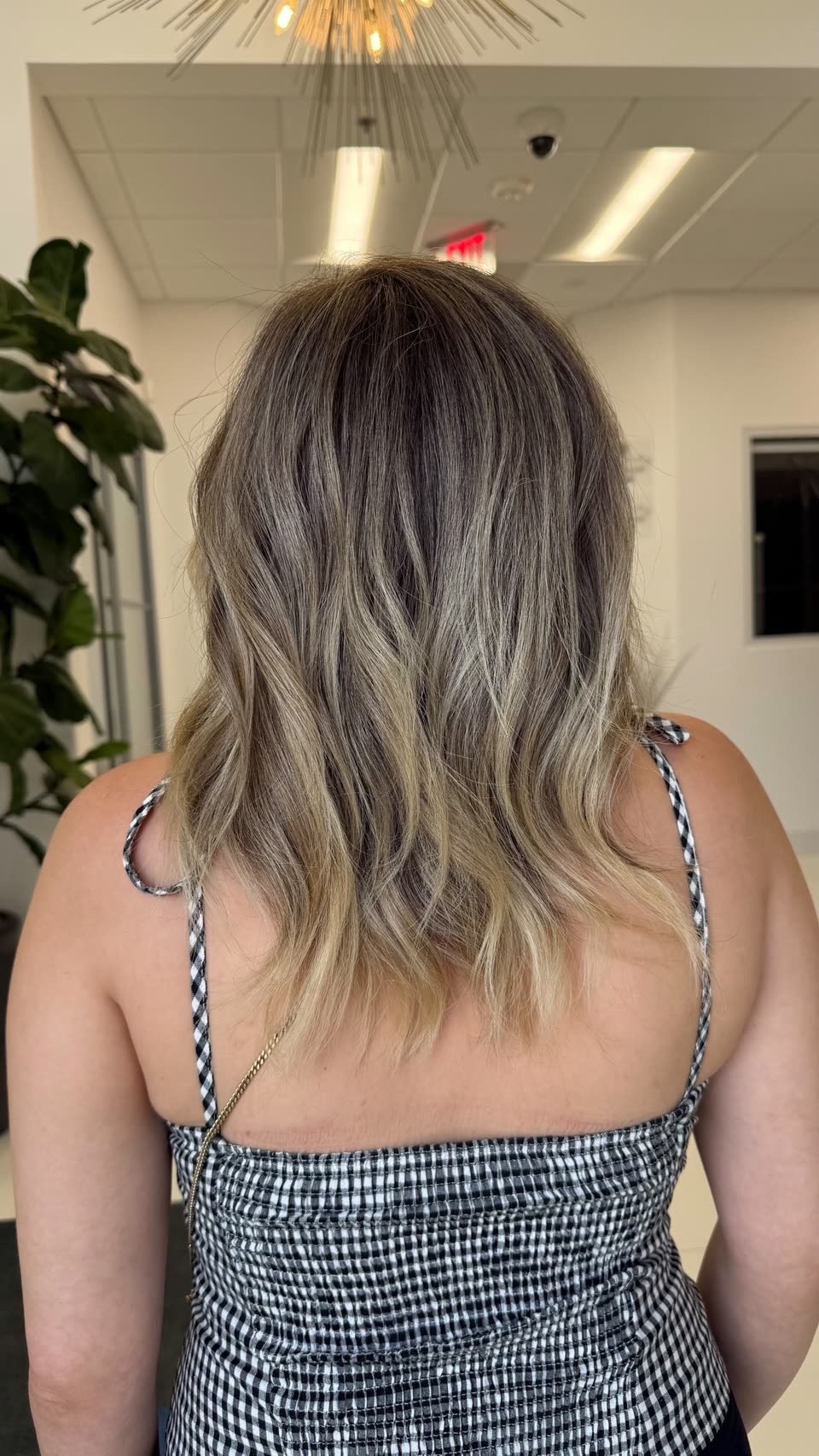 Shoulder-length hair blending from an ash-brown root into soft blonde ends, in loose waves, seen from behind