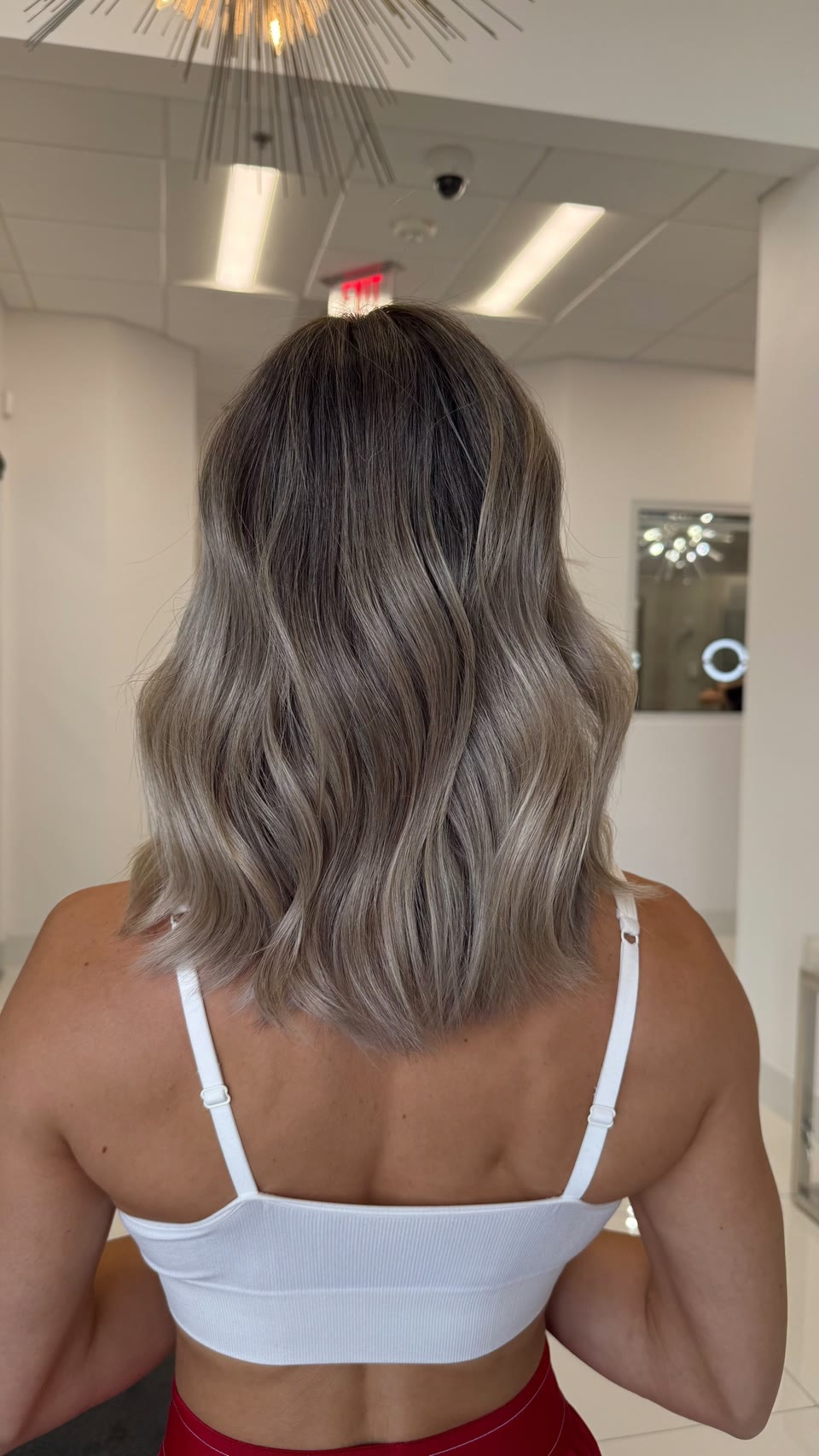 Shoulder-length ash-blonde waves with a deeper root, seen from behind