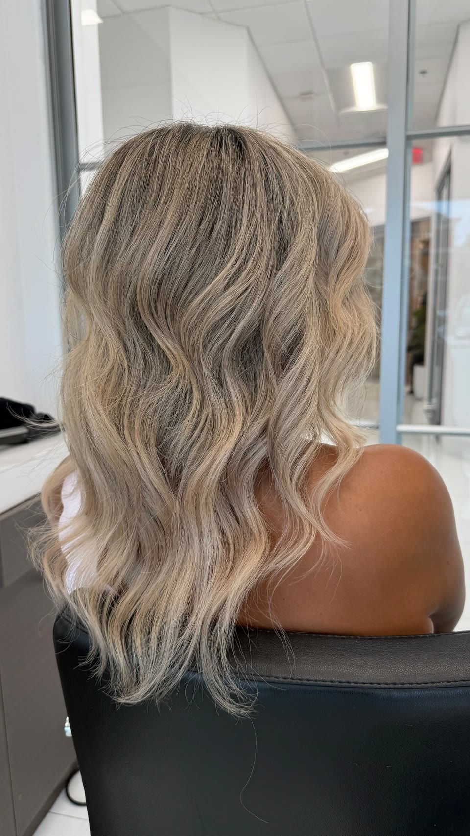 Mid-length, layered beige-blonde waves with a shadow root, seen from behind