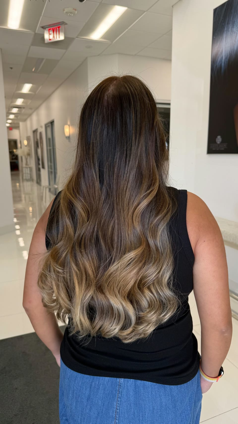 Long brunette balayage blending into caramel-blonde ends, in loose waves, seen from behind